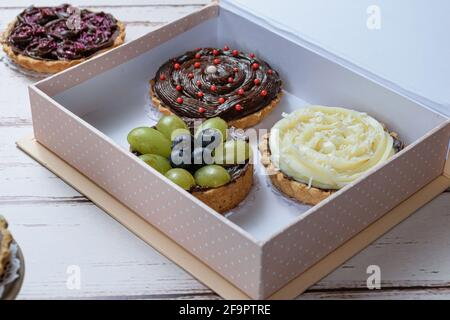 Gros plan de tarte avec pâte de beurre farcie de ganache de chocolat, décorée de raisins verts et de bleuets. À l'intérieur d'une boîte cadeau et avec d'autres chaussons. Banque D'Images