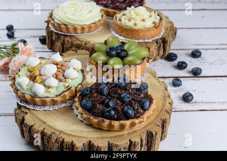 Tarte à la pâte de beurre farcie de ganache au chocolat, décorée de mertilos. Sur une plaque en bois et entourée d'autres tourtes. Banque D'Images