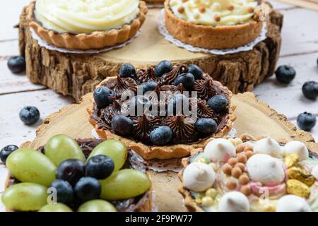 Gros plan de tarte avec pâte de beurre farcie de ganache de chocolat, décorée de mertilos. Sur une plaque en bois et entourée d'autres tourtes (vue latérale). Banque D'Images