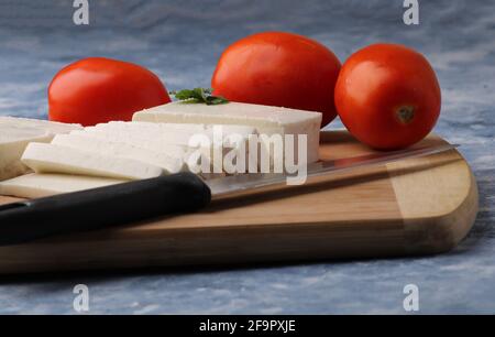 tranché de paneer frais ou de fromage cottage avec tomates et couteau sur la planche à découper. Banque D'Images