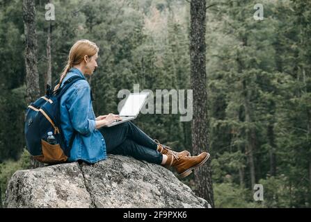 Jeune femme assise sur terre à la forêt et travaillant sur ordinateur portable . Banque D'Images