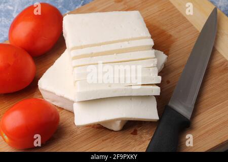 tranché de paneer frais ou de fromage cottage avec tomates et couteau sur la planche à découper. Banque D'Images