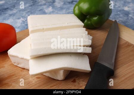 Paneer ou fromage cottage avec tomates, poivrons et un couteau sur une planche à découper en bois. Banque D'Images