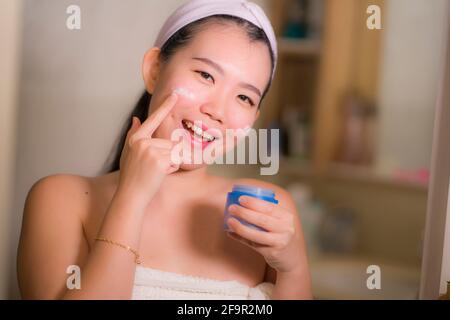 Portrait de jeune heureuse et belle femme japonaise asiatique appliquant crème et sérum anti-rides pour le visage au miroir de salle de bains soins de la peau et beauté tre Banque D'Images