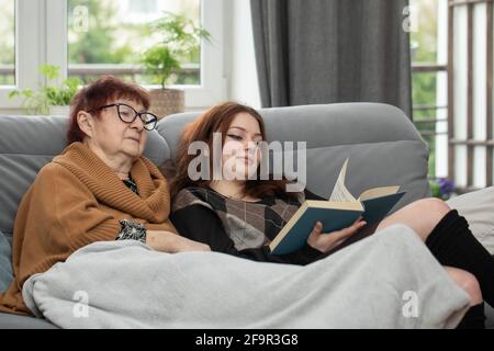 Une femme âgée et une adolescente lisent ensemble un livre. Grand-mère et petite-fille lisant le livre ensemble à la maison. Banque D'Images