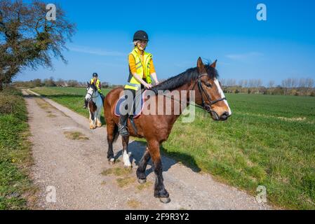 Des jeunes femmes qui font des chevaux sur un sentier de campagne à travers la campagne par une journée ensoleillée au printemps à West Sussex, au Royaume-Uni. Promenade à cheval / cavaliers. Banque D'Images