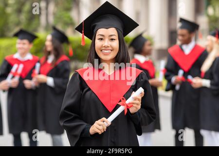 Bonne femme asiatique étudiante en gaiement posant pendant la cérémonie de remise des diplômes Banque D'Images