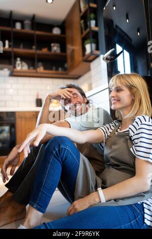 Les jeunes professionnels fatigué couple sitting on plancher de la cuisine après la cuisson Banque D'Images