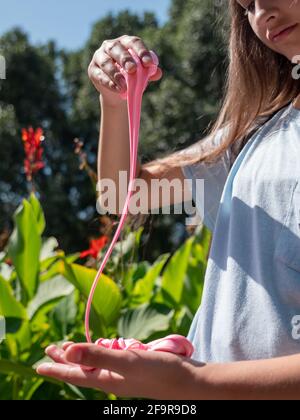 Jeune fille enfant tenant et jouant avec de la chaux rose douce et moelleuse dans un parc de la ville par une journée ensoleillée. Fleurs rouges et plantes vertes sur le fond. Banque D'Images