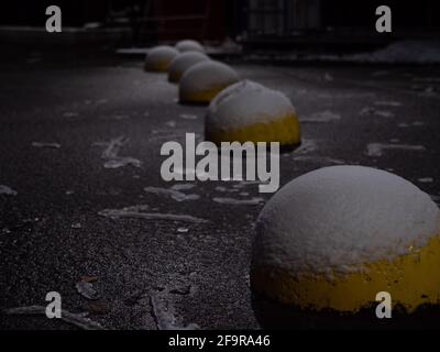 Bollards en béton jaune anti-stationnement en forme d'hémisphère couverts de neige et de glace. En route pendant une nuit d'hiver. Banque D'Images