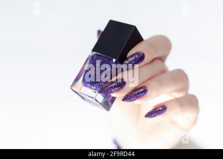 Main femelle avec de longs ongles et manucure au lilas violet contient une bouteille de vernis à ongles Banque D'Images