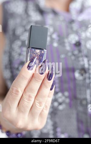 Main femelle avec de longs ongles et manucure au lilas violet contient une bouteille de vernis à ongles Banque D'Images