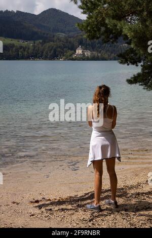 Jeune randonneur femelle debout sur la rive du lac Fuschl regardant l'hôtel Schloss Fuschl à Fuschl,Salzbourg, Salzkammergut,Autriche,Europe. Banque D'Images