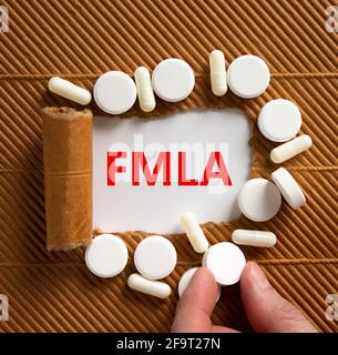 FMLA, symbole de congé médical familial. Les mots « FMLA, Family Medical Leave Act » apparaissent derrière un papier brun déchiré. Pilules blanches, main de docteur. Médical et Banque D'Images