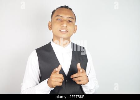 Jeune homme d'Asie du Sud portant une chemise blanche et un gilet pointant vers la caméra sur fond blanc Banque D'Images