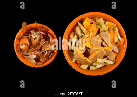 Déchets biologiques de cuisine de légumes et de fruits dans des bols d'orange, isolés sur le noir. Banque D'Images