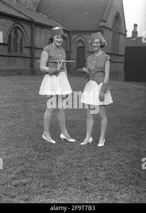 1956, historique, à l'extérieur dans le domaine de l'église, debout pour leur photo, deux jeunes dames dans leurs costumes pour la traditionnelle procession de la Reine de mai, Angleterre, Royaume-Uni. Dans de nombreux villages anglais, les célébrations du jour de mai ont impliqué le couronnement d'une reine de mai et la danse autour d'un Maypole, activités qui ont eu lieu en Angleterre pendant des siècles. Sélectionné parmi les filles de la région, la Reine de mai portant une couronne, commencerait la procession et le défilé de chars et de danse. Dans le nord industrialisé de l'Angleterre, les écoles du dimanche de l'Église ont souvent dirigé l'organisation de la journée. Banque D'Images