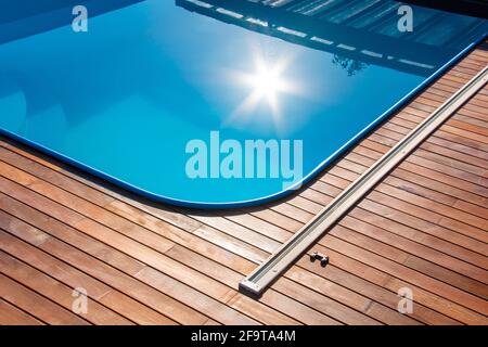 Terrasse en bois IPE autour de la piscine, bord de la piscine extérieure avec reflet de soleil sur l'eau bleue, terrasse en bois tropical de gros plan Banque D'Images