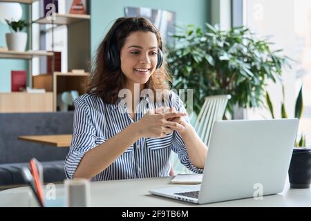 Jeune étudiante hispanique dans un casque parlant chat en ligne à l'aide d'un ordinateur portable. Banque D'Images