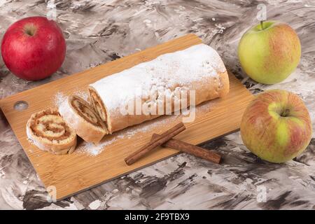 Rouleau de pommes ou strudel sur une planche à découper, bâtonnets de cannelle et pommes fraîches. Un rouleau de pommes fait maison. Banque D'Images