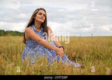 belle jeune femme est assise dans un pré en fleurs une journée d'été ensoleillée et sourires Banque D'Images