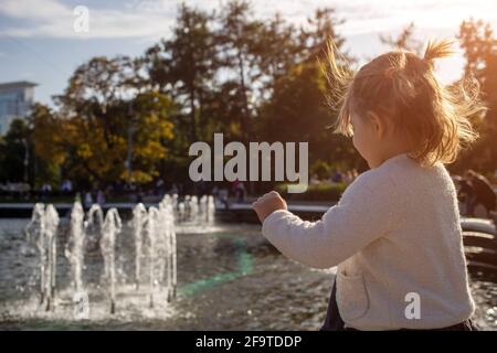 adorable petite fille regarde la fontaine. enfant dans un parc avec des fontaines par temps ensoleillé. week-end en famille petite fille regardant dans une fontaine dans le th Banque D'Images