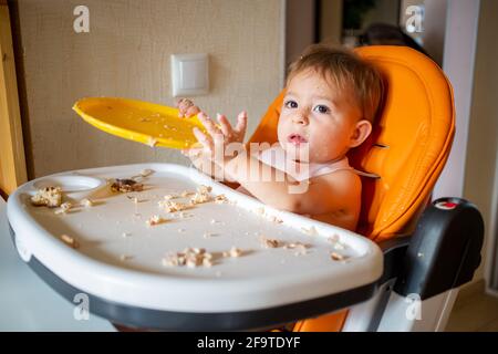 bébé adorable joue avec une assiette à la table. petit enfant s'indulge dans une chaise de bébé après avoir mangé Banque D'Images