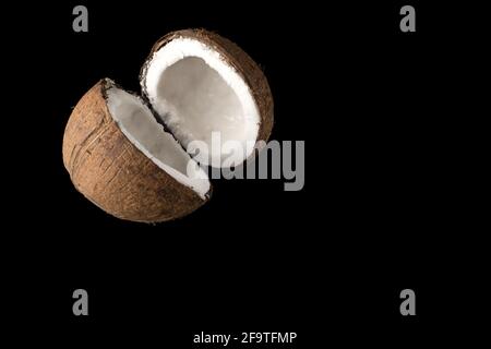Une noix de coco mûre divisée en deux parties, sur fond noir Banque D'Images