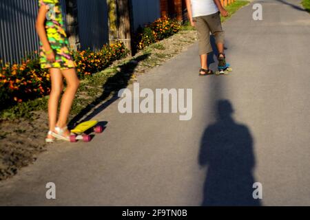 Refocalisez les petits enfants avec la planche à roulettes Penny sur la piste du parc. Garçon et fille manne un panneau de penny par jour de soleil. Une image de style de vie en plein air sous un soleil Banque D'Images