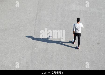 VIENNE, AUTRICHE - 28 AOÛT 2018 : jeune homme solitaire non identifié marchant et son ombre sur une surface asphaltée, vue d'un point plus élevé. Banque D'Images