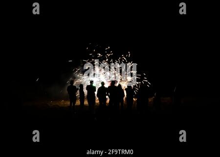 Groupe de personnes en silhouette regarder les feux d'artifice exploser sur la plage dans l'obscurité totale. Banque D'Images