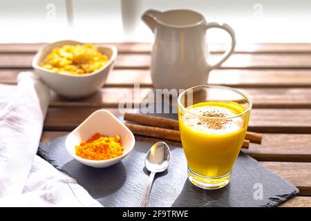 foyer sélectif d'un petit déjeuner de lait doré avec curcuma et de la cannelle dans un verre placé sur un tableau d'ardoise et des cornflakes dans l'arrière-plan d'une table Banque D'Images