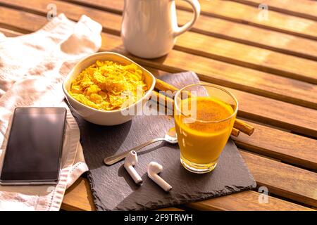 Petit déjeuner sélectif sur table en bois avec casque pour téléphone portable avec du lait doré accompagné de curcuma et de cannelle Céréales foo indien Banque D'Images