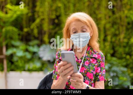 Portrait à l'extérieur d'une femme touriste âgée portant un visage médical jetable masque et utilisation du téléphone portable pendant l'été Banque D'Images