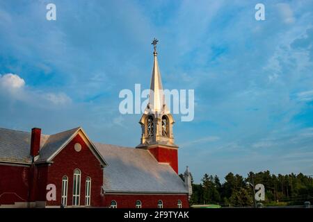 Église de campagne en brique rouge avec un clocher argenté sous un ciel bleu vif Banque D'Images