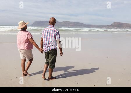 Couple afro-américain senior tenant les mains marchant sur la plage Banque D'Images