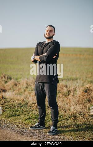 Photo verticale d'un jeune homme caucasien barbu habillé nad noire debout dans une posture assurée Banque D'Images