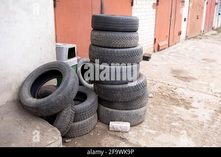 Pile de vieux pneus de voiture contre le mur de brique de service de pneus ou de garage. Pollution, recyclage et réchauffement de la planète. Banque D'Images