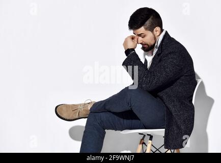 Homme barbu réfléchi en Jean et veste en tweed décontractée est se place à côté de l'appareil photo en tenant la main sur son front en pensant Banque D'Images