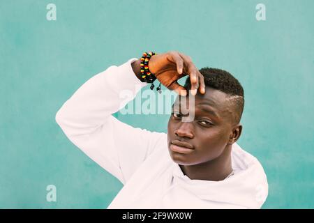 Portrait d'un jeune homme noir africain avec des cheveux afro contre un mur vert portant un sweat-shirt blanc avec sa main sur son visage. Diversité et cont. Ethniques Banque D'Images