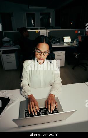 Portrait d'une jeune femme de direction portant des lunettes de vue dactylographiant dessus ordinateur portable sur le lieu de travail Banque D'Images