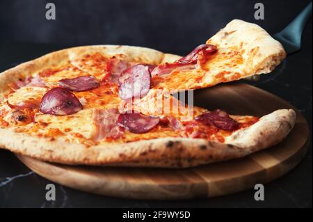 Délicieuse pizza maison sur une assiette en bois contre le noir arrière-plan Banque D'Images