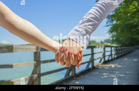 Gros plan d'un couple mignon tenant les mains et marchant sur un pont en bois au-dessus d'un lac Banque D'Images