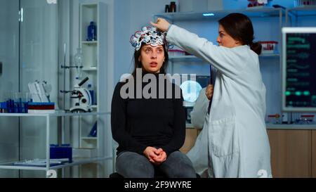 Médecin chercheur en ajustant le casque EEG en analysant l'évolution du patient après le traitement contre une maladie du système nerveux. Équipe de scientifiques travaillant tard dans la nuit en laboratoire de recherche neurologique Banque D'Images