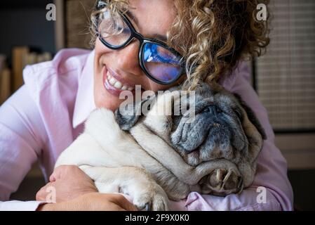Une femme heureuse embrasse son chien pug avec amour et amitié. Concept de meilleur ami pour toujours et propriétaire d'animal appréciant le temps à la maison - gros plan de l'affection an