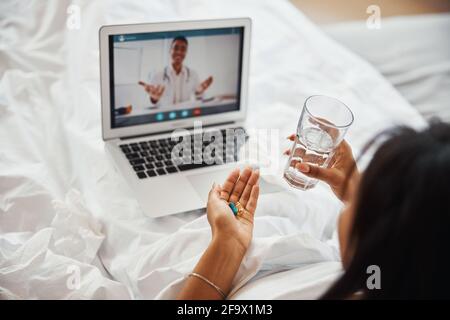 Jeune femme prenant des pilules et ayant la consultation en ligne avec le médecin Banque D'Images