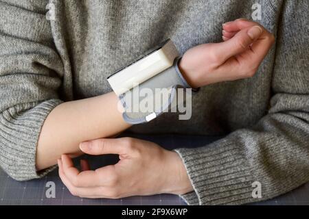 Utilisation du tensiomètre au poignet. Les mains des femmes se rapprochent. La femme se mesure elle-même la pression artérielle avec le tonomètre sur son poignet. Banque D'Images