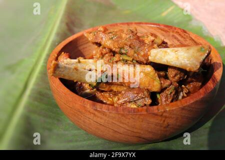 Curry de côtelettes de mouton. Curry de viande de chèvre non végétarienne, épicé et rustique indien. Servi dans un bol en bois sur fond de feuilles de banane. Espace réservé aux copies. Banque D'Images