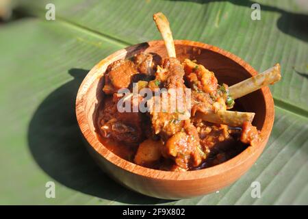 Curry de côtelettes de mouton. Curry de viande de chèvre non végétarienne, épicé et rustique indien. Servi dans un bol en bois sur fond de feuilles de banane. Espace réservé aux copies. Banque D'Images