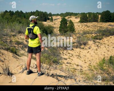 Athlète coureur surplombant le désert. Course à pied à travers le pays. L'homme porte des vêtements de sport, un t-shirt jaune, un short et une veste Banque D'Images